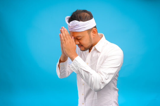Handsome young Balinese man wearing Indonesian traditional udeng doing greeting or welcome gesture.