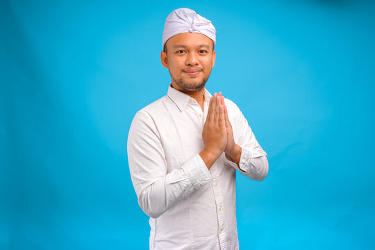 Handsome young Balinese man wearing Indonesian traditional udeng doing greeting or welcome gesture.