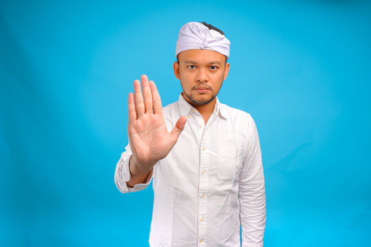 Serious young Balinese man wearing traditional udeng doing rejection or stop hand gesture.