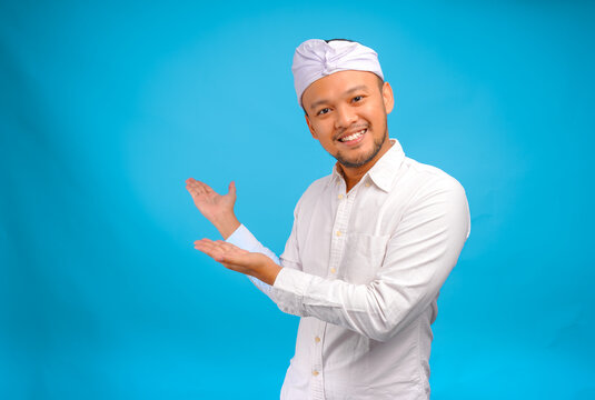 Joyful young Balinese man wearing Indonesian traditional udeng doing inviting gesture.