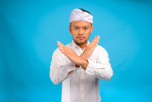 Serious young Balinese man wearing traditional udeng doing rejection or stop hand gesture.