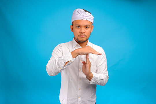 Calm young Balinese man wearing Indonesian traditional udeng doing time out gesture with hands.