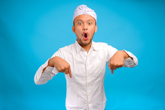 Shocked Balinese man wearing Indonesian traditional udeng pointing up to the copy space downwards.