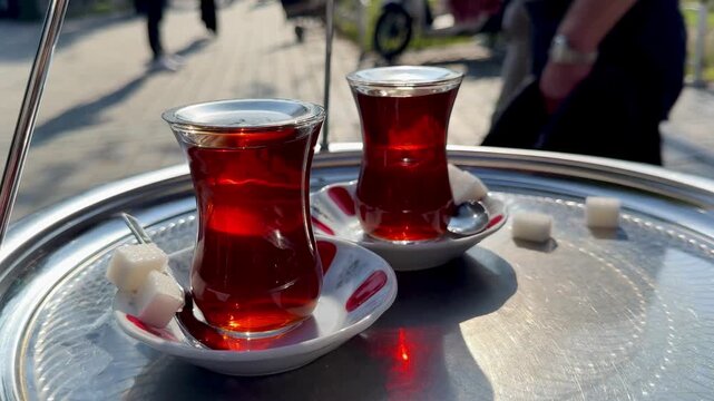 Two traditional tulip-shaped glasses of hot Turkish black tea on a silver tray. Authentic tea service in Istanbul with sugar cubes. Concept of Turkish hospitality and street cafe culture.