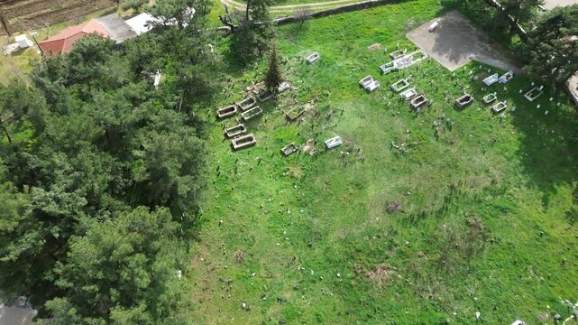 Top-down aerial drone shot of a small Muslim cemetery located in a lush green field next to a mosque. The footage shows traditional graves in the village of Mischos, Komotini, Greece, surrounded by ta