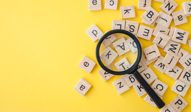 Magnifying glass with wooden English alphabet letters on yellow background, concept for grammar and thinking development