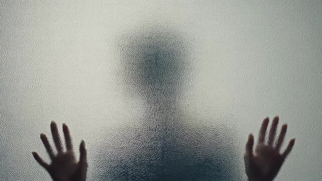 Silhouette of a person's head and hands pressed against frosted glass