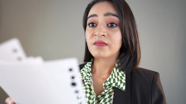 Close up of stressed exhausted working young Asian business woman manager female boss hold document papers report overworked looking at camera feels anxiety, isolated over grey studio background.