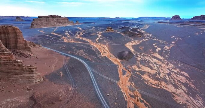 Aerial view of a remote road winding through vast yardang landforms and dark gravel desert in Xinjiang, China.