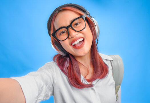 Happy young Asian girl in white shirt is posing to the camera and taking a selfie picture.