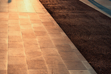 Sunlight bathes an urban sidewalk and dark asphalt road in warm golden light. Textured background for modern designs, copy space