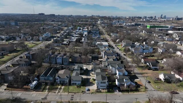Aerial winter view of Nashville residential neighborhood with rows of single-family homes, suburban streets and downtown skyline visible in distance under clear daylight. Sunlight in January.