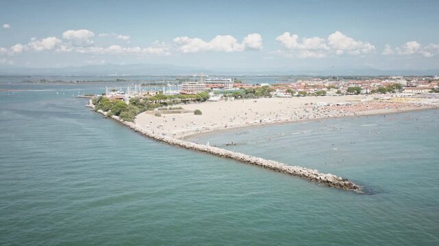 Stunning 4K UHD drone orbit shot circling the stone pier and sandy beach of Grado, Italy, during a bright summer day. Perfect for cinematic travel vlogs and tourism marketing.