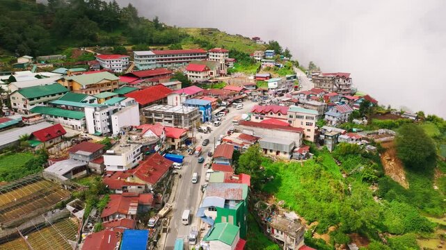 Drone moves forward above Atok mountain town lit by sun through drifting rain