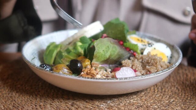 Close up of person using fork to eat healthy vegetable bowl with quinoa avocado and boiled eggs