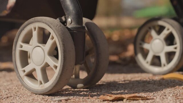 Closeup stroller wheels on gravel, detailed rubber tread and wheel rotation, mud specks and textured frame, steady motion across park trail, subtle sunlight and shadow, marriage symbolism of shared