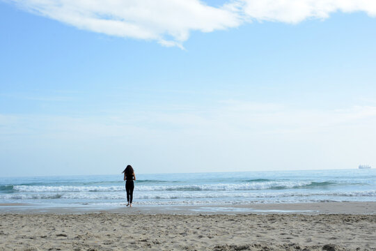 A lonely girl walks along the seashore. A female silhouette against the sea.