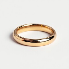 A simple, gold band ring rests on a white surface, reflecting light with its smooth surface