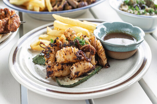 mediterranean style grilled squid with escabeche sauce and fries on white table at ibiza spain restaurant