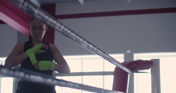 Focused and determined, the woman boxer wraps her hands tightly and correctly, prioritizing injury prevention before diving into a demanding boxing workout.