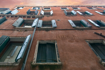 Red Venetian facade with open green shutters under sunset sky © Sergey