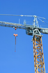 Naklejka premium A tall yellow and light blue construction crane stands prominently against a clear and bright blue sky showing its detailed metal lattice structure and hoisting mechanism