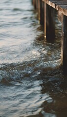 Fototapeta premium Tranquil summer waves softly meet an old wooden pier bathed in golden hour light serenity