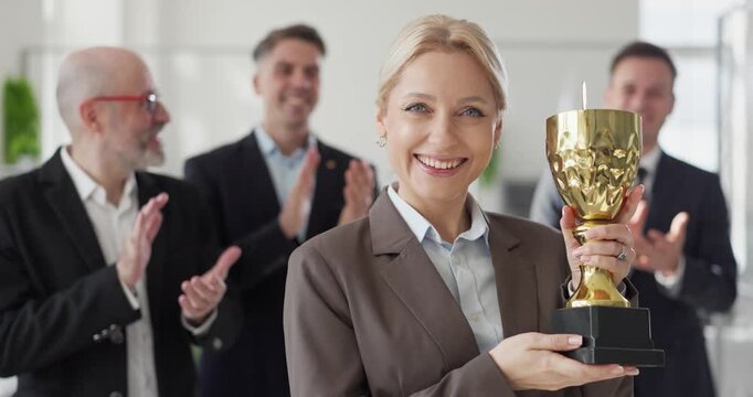 Businesswoman winner holds trophy amid team applause. In the office colleagues applaud the leader for a hard earned award and visible success. Clear celebration of business achievement.