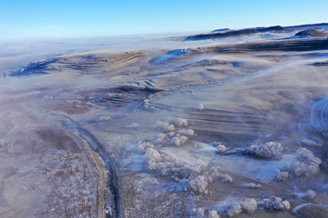 Fototapeta premium Aerial view of misty countryside hills at wintertime, morning fog above