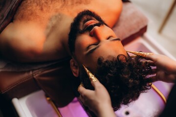 Man receiving relaxing hair wash treatment in salon. Japanese spa head