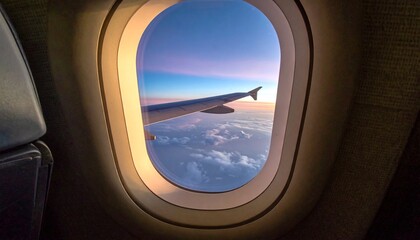 Naklejka premium Airplane window view of wing, clouds, and sky at sunset.