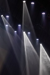 Naklejka premium Bright stage spotlights shine downward through swirling theatrical smoke in a dark performance venue, creating dramatic beams of light with strong contrast and atmospheric lighting