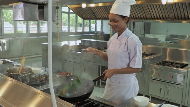 Smiling female chef cooking wok professional commercial kitchen. Skilled cook tossing ingredients in frying pan steam focuson culinary expertise restaurant service, and hospitality industry concept.