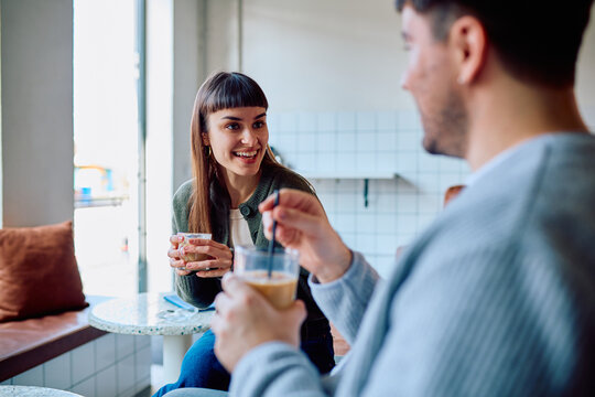 Young couple enjoying a friendly social interaction, drinking coffee and smiling during a casual date in a modern cafe
