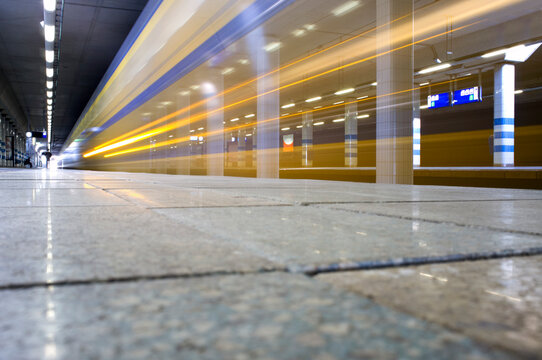 A train passing through a station, surface view, a trail of lights and motion blur.