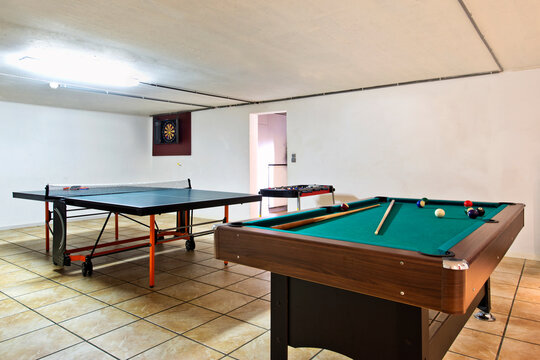 Interior view of a basement room with pool billiard and ping pong tables.