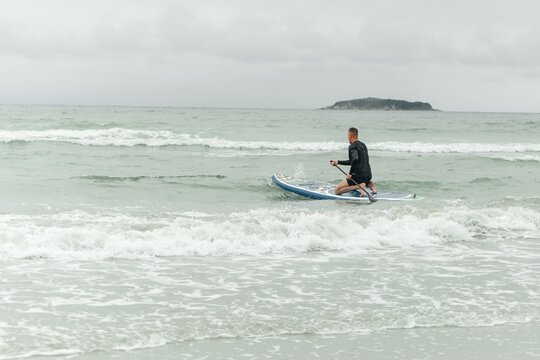Man kneeling on paddleboard in the ocean waves.