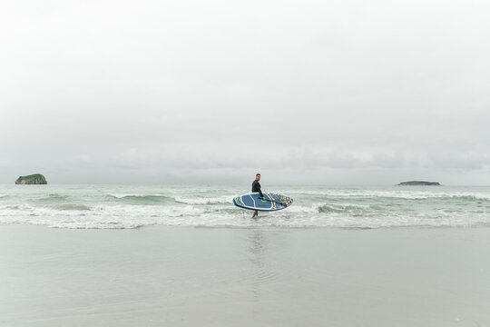 Man holding paddleboard, standing in shallow water.