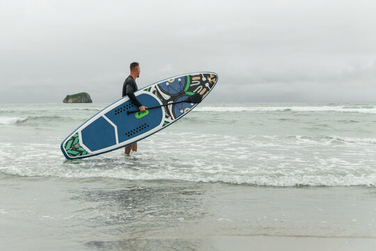 Surfer entering the ocean with paddleboard on overcast day.