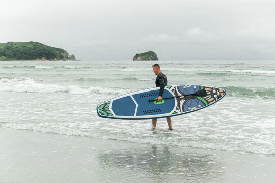 Man carrying paddleboard out of the sea.