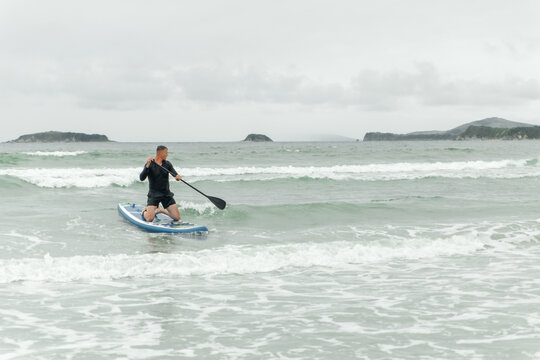 Man paddling on knees on paddleboard in the sea.