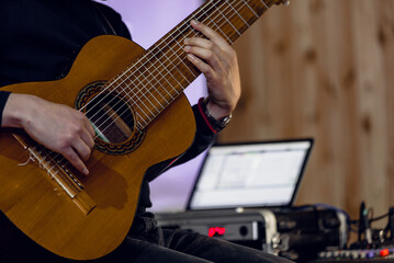 Fototapeta premium Closeup photo of young man playing on electric guitar in sound recording studio Detailed view of ten-string nylon guitar during live studio performance