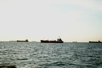 Obraz premium Large cargo ship sailing on the sea during sunset with distant ships and mountains on the horizon, showing maritime transportation and ocean travel