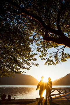 Backlit couple standing by lake Crescent at sunset, Olympic National Park.