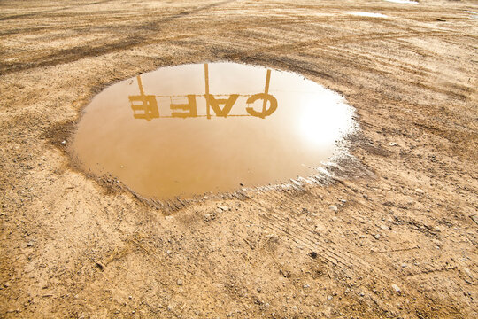 Cafe sign reflection in puddle of water on the ground in the dirt.