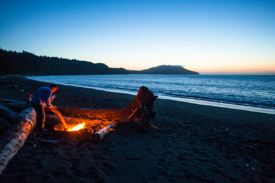 Beach camp fire on Puget Sound, glowing embers of logs at dusk.