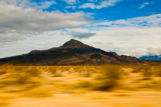 View across a desert landscape to a sharp peak, seen from a moving vehicle.