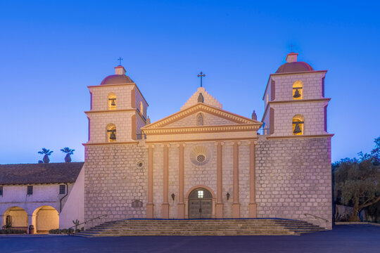 Santa Barbara mission, an 18th century Spanish colonial style church building at dusk, pediment and bell towers.