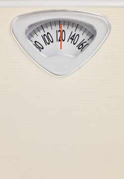 Analog bathroom scale close-up with red needle pointing at 120 pounds. Health and weight loss concept on neutral background.