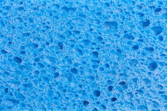 Close up full frame of a blue cleaning sponge with a pitted porous surface, a plastic household object.